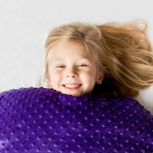 young girl smiling under a purple weighted blanket
